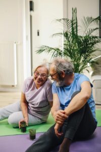 Elderly couple sitting on yoga mats, smiling with green smoothies, promoting healthy living.