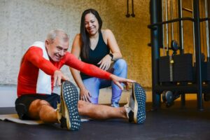 Elderly man in a gym stretching with a fitness coach, promoting a healthy lifestyle.